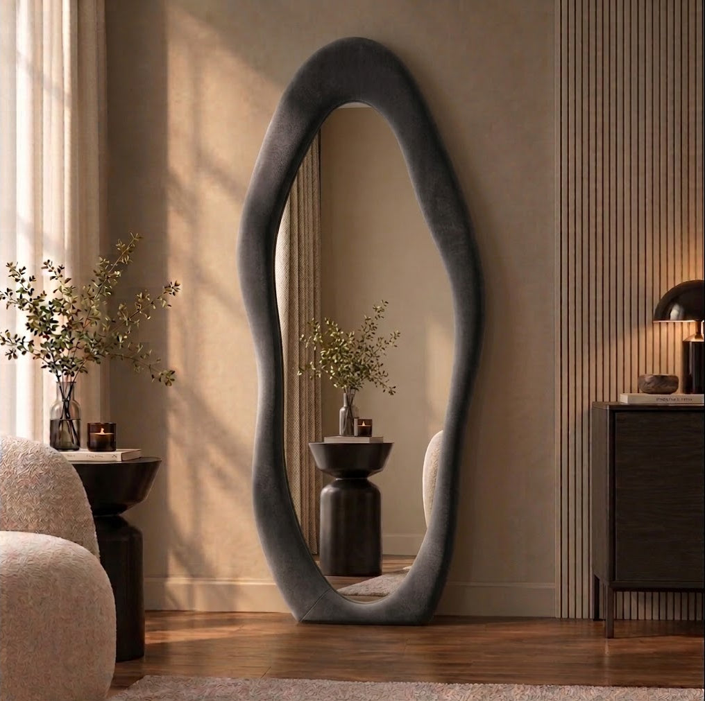 Dark gray wavy flannel-framed floor mirror leaning beside a wood-slat wall, reflecting a vase on a side table.